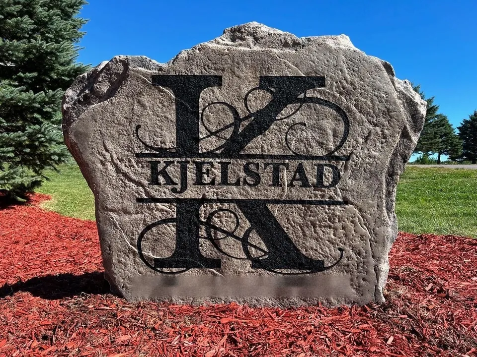 Grey address boulder with a large engraved monogram set in red mulch