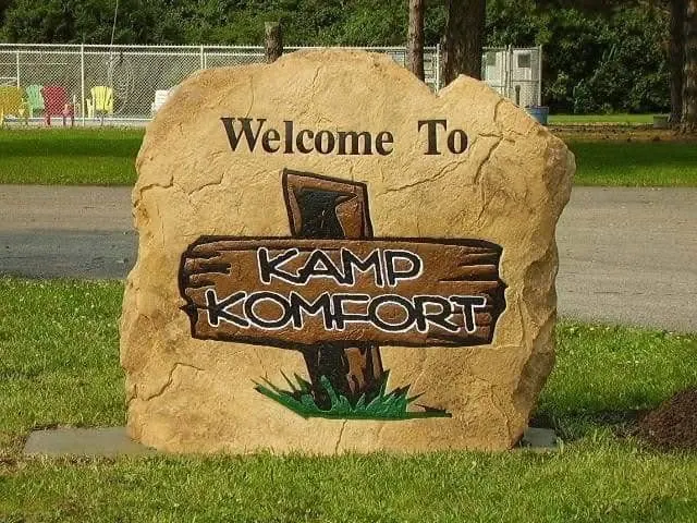 Tan campground welcome boulder with a wooden-sign style graphic and colored lettering