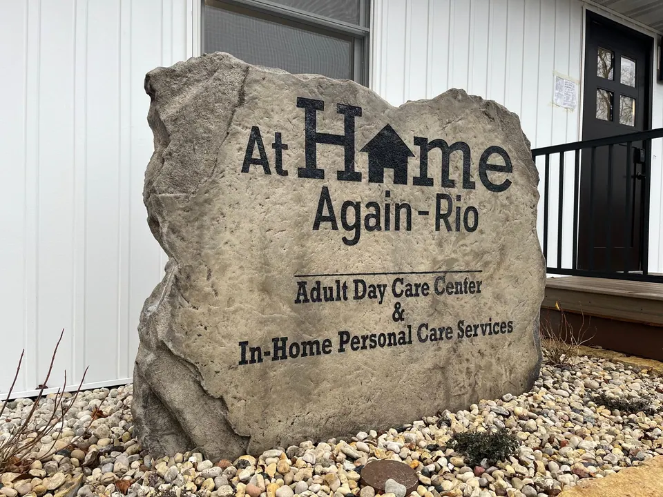 Engraved boulder sign for an adult day care center with a house logo, set in a stone bed by the entrance