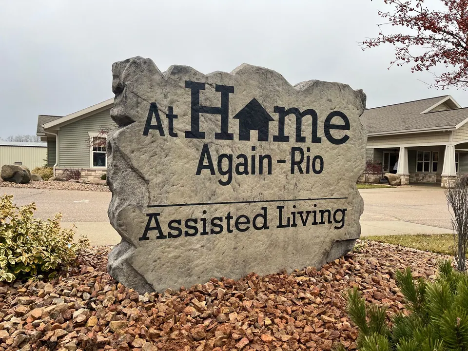 Engraved assisted living boulder sign with a house logo in a landscaped bed