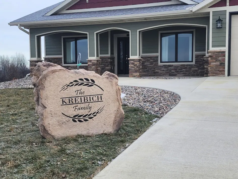 Tan family-name boulder with a wheat wreath design in a landscaped front yard