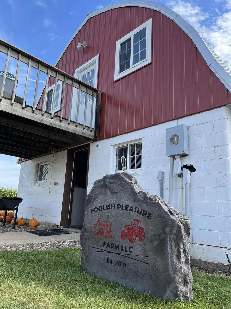 Grey farm sign boulder with red tractor artwork set beside a red barn