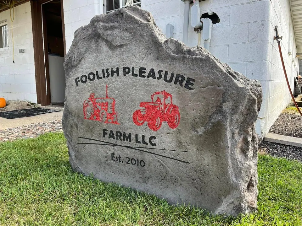 Grey farm sign boulder with red tractor artwork and an established date, set on the lawn