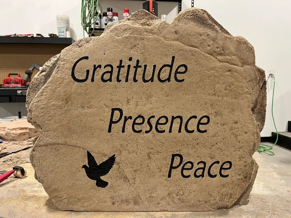 Garden boulder engraved with the words gratitude, presence and peace and a dove