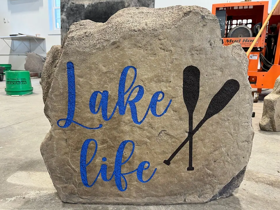 Tan "Lake life" boulder with blue script lettering and a canoe paddle