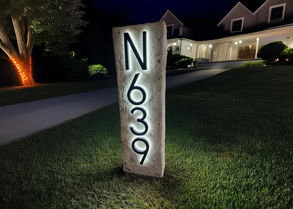 Tall address column boulder with backlit house numbers glowing at night