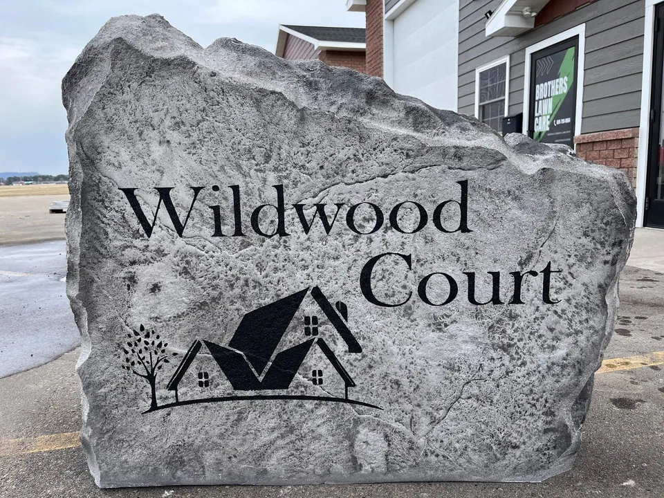 Grey neighborhood entrance boulder engraved with the street name and a house and tree design