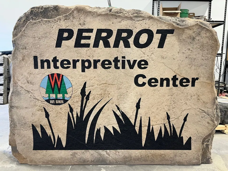 Large tan boulder sign for a state park interpretive center with bold lettering, a full-color park logo and prairie grass silhouette