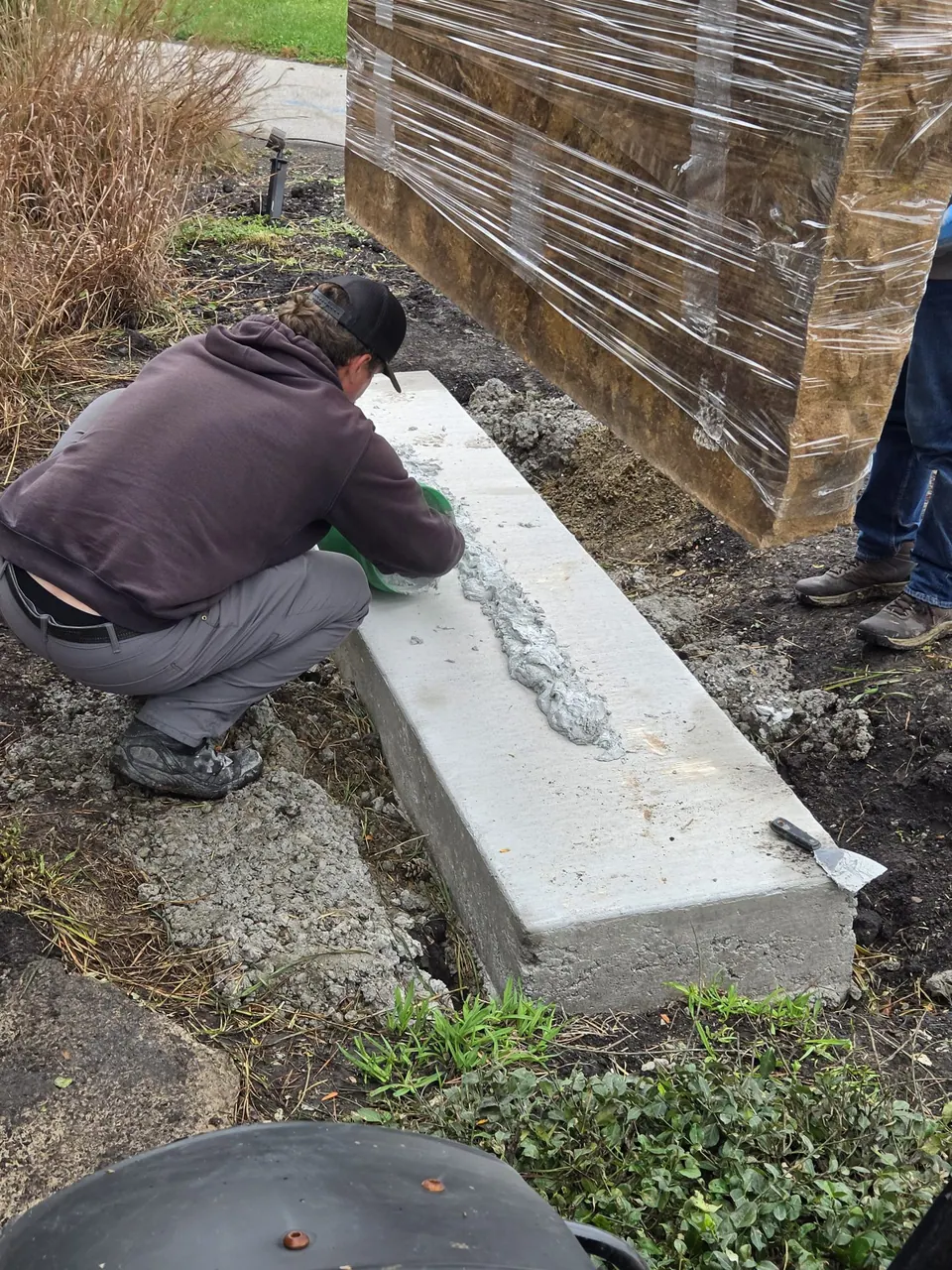 Crew member working on the concrete footing beside the wrapped boulder
