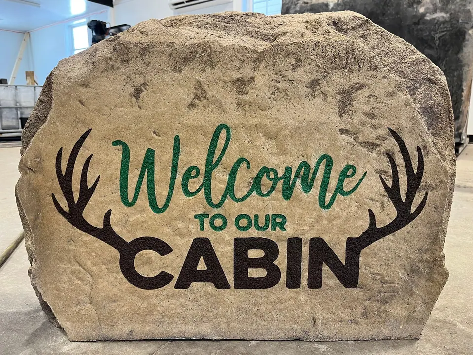 Tan cabin welcome boulder with green script lettering and deer antlers