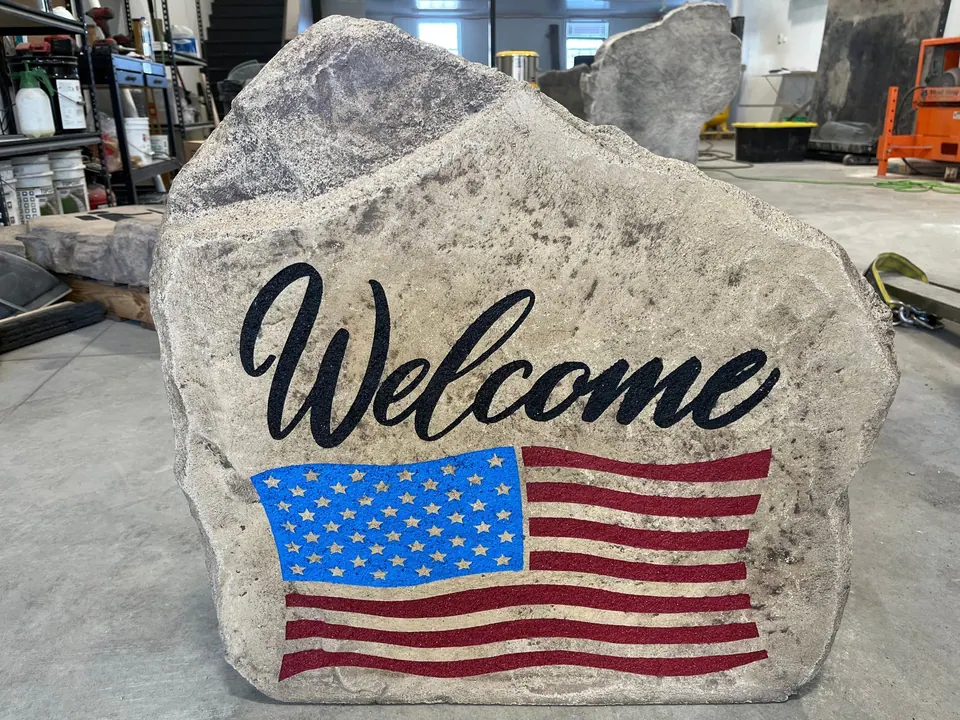 Welcome boulder with script lettering and a full-color American flag